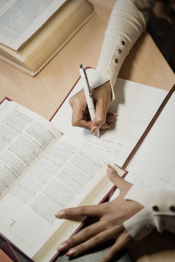 Close-up of hands writing notes while studying books, emphasizing education and learning.